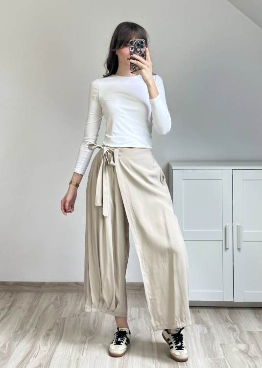 Beżowe spodnie kopertowe z szeroką nogawką i wiązaniem w talii stylizacja codzienna Spodnie kopertowe beżowe z asymetrycznym krojem i luźnym fasonem outfit minimalistyczny